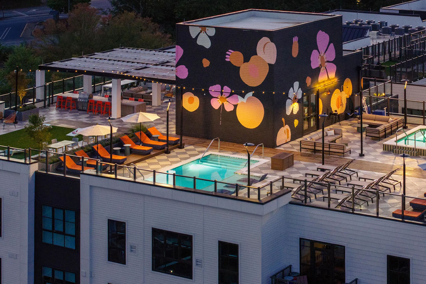 Rooftop pool at night with shaded seating, lounge areas, and a poolside mural.